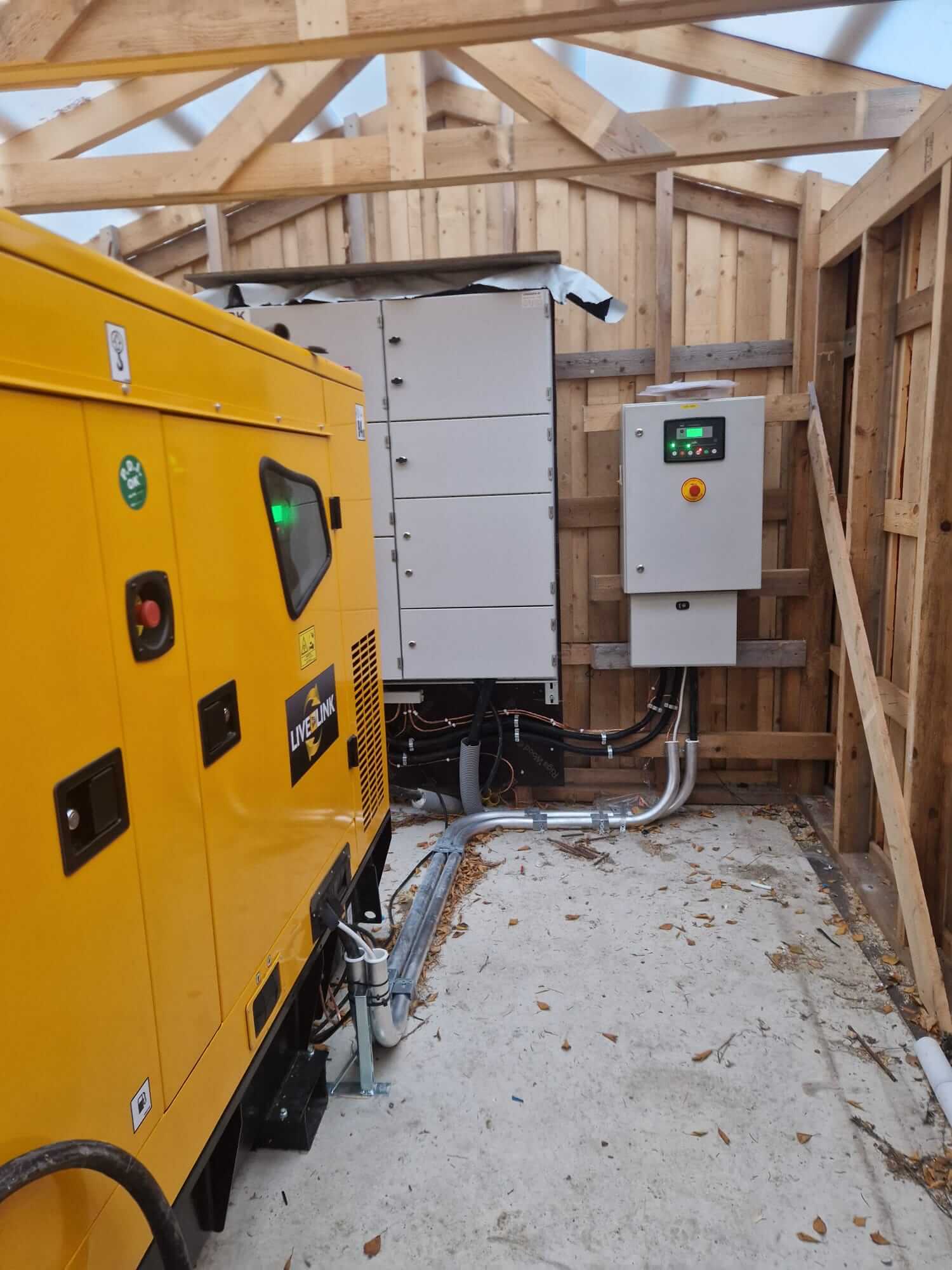 Keltainen generaattori ja sähkötaulut puurunkoisessa tilassa betonilattialla.